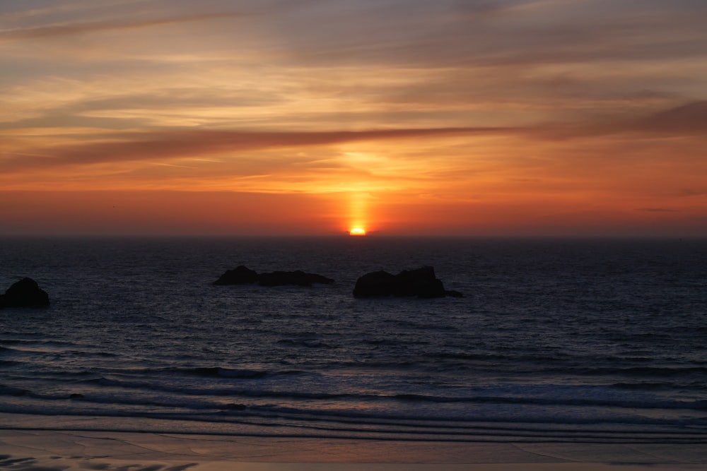 silhouette of rock formation on sea during sunset