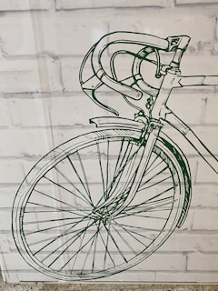 A detailed green line drawing of a bicycle's front half, including the handlebars, wheel, and part of the frame, is displayed against a white brick wall background.