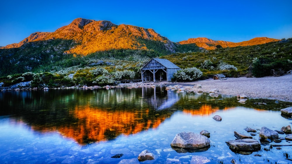 Casa de madera marrón en el lago cerca de la montaña marrón bajo el cielo azul durante el día