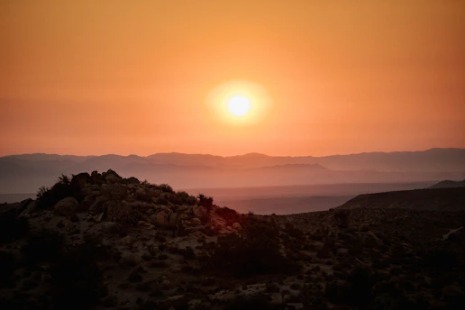 A golden sunset over the rugged red landscapes of the Australian Outback, casting long shadows among ancient rock formations.
