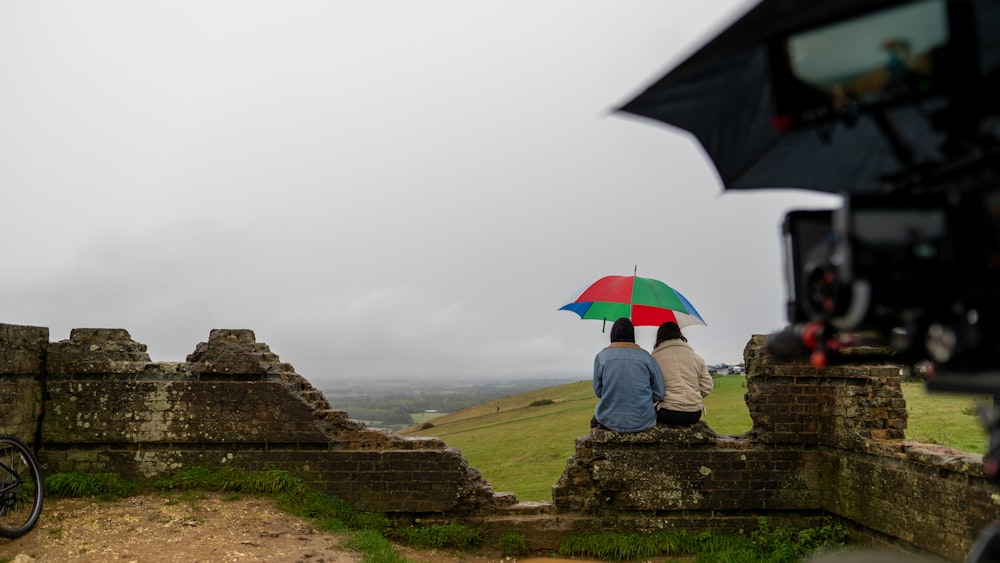 person sitting on rock near red umbrella during foggy weather