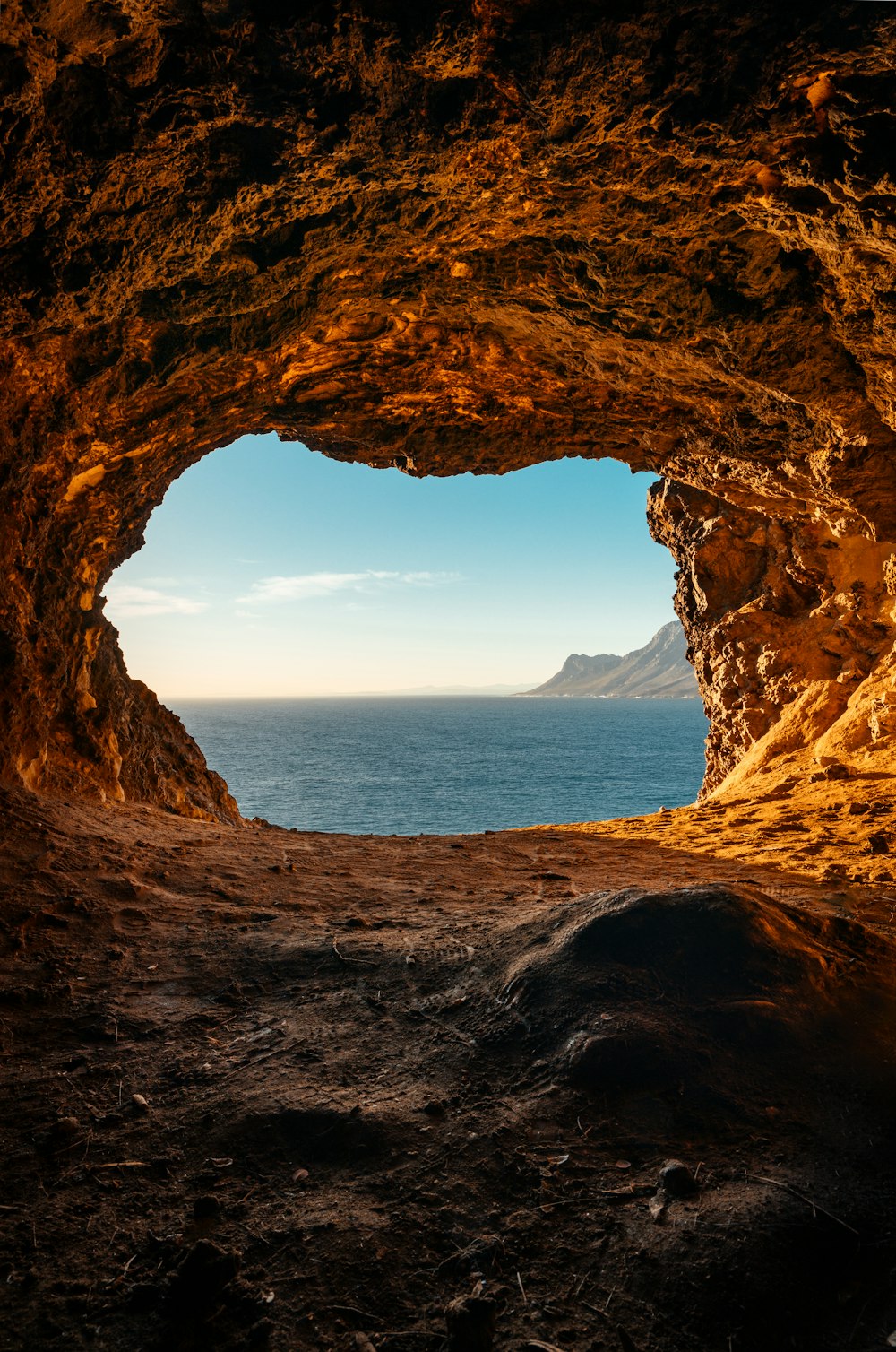 brown cave near body of water during daytime