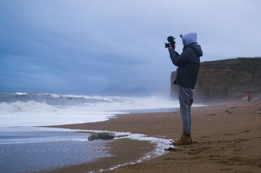 昼間の波の写真を撮る黒いジャケットの男性