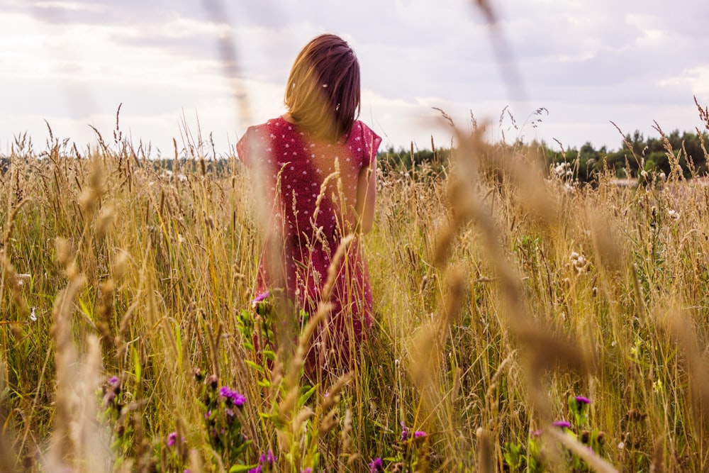 femme en robe rose debout sur le champ d’herbe verte pendant la journée