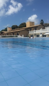 A large hotel pool filled with crystal-clear water under bright sunlight.
