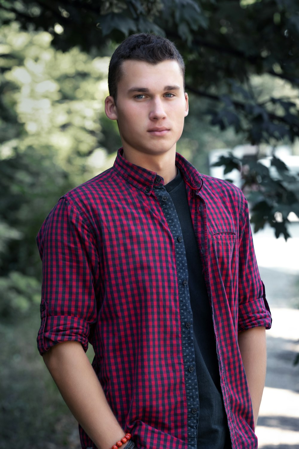 boy in red and black plaid button up shirt standing near green trees during daytime