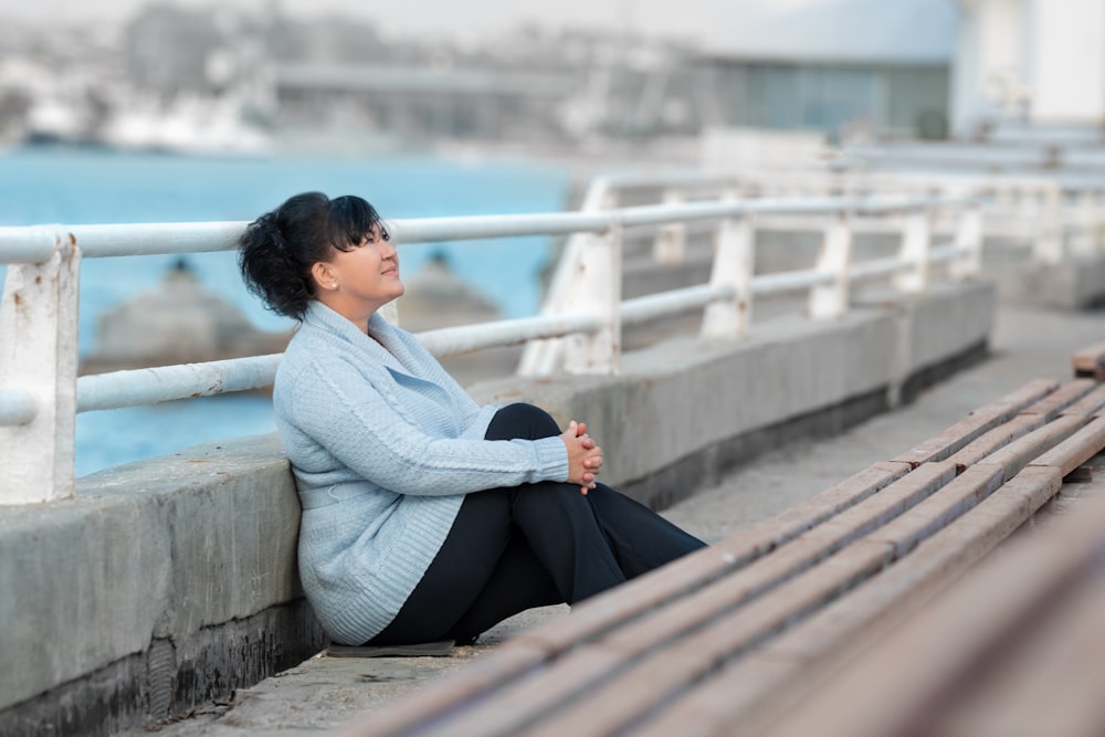 woman in white sweater and black pants sitting on concrete bench during daytime