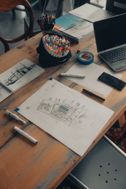 A cozy studio workspace with sketches, colorful indexes, and design tools scattered on a wooden table.