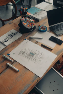 A cozy creative workspace with art supplies, sketches, and a laptop open to a project plan.