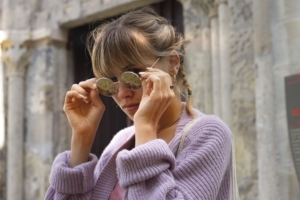 woman in purple sweater holding her sunglasses