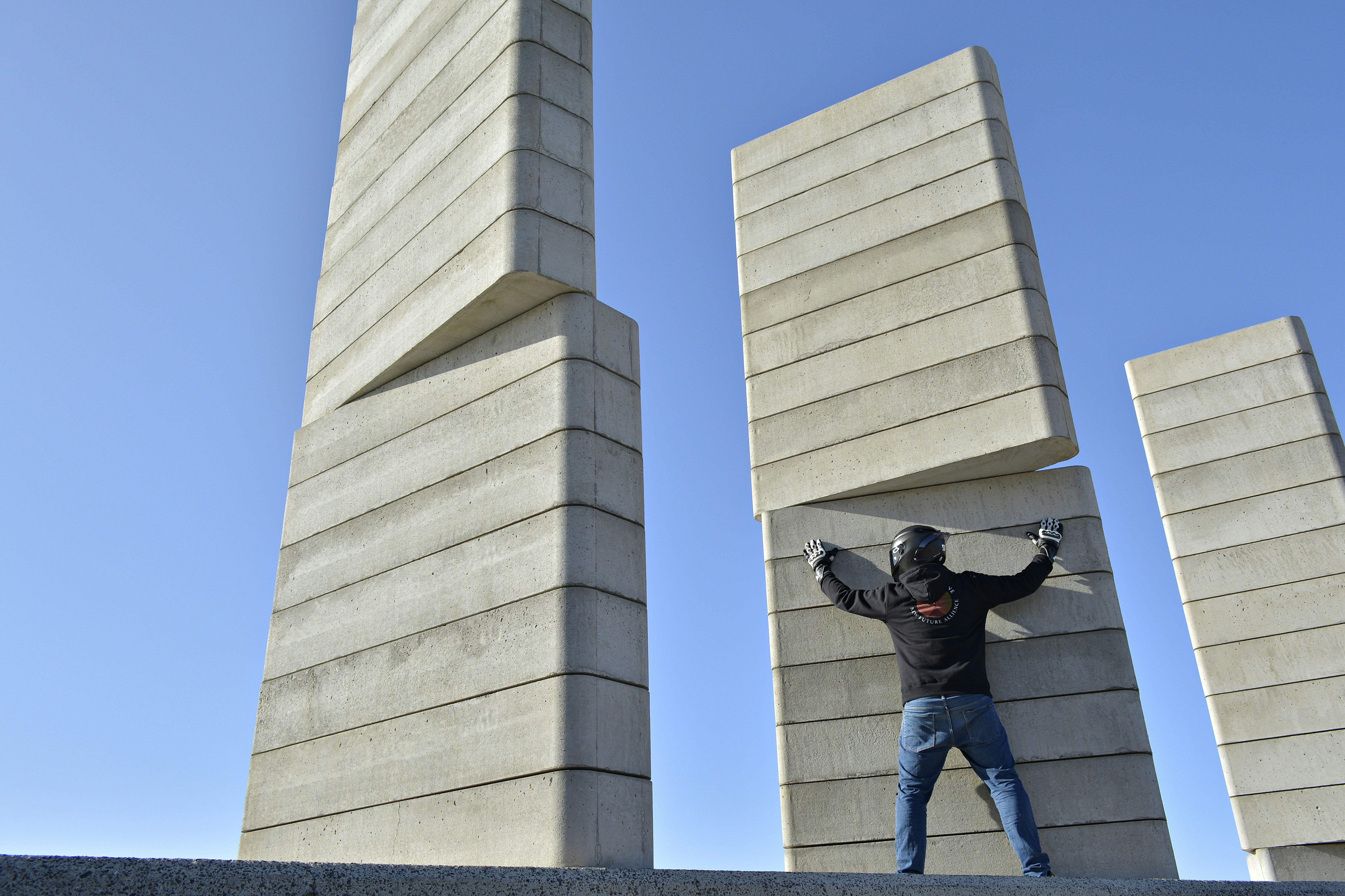 man in black jacket and blue denim jeans standing on white concrete building during daytime