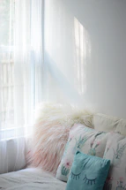 A cozy corner with a floral decor pillow and a sheer curtain softly lit by natural light.