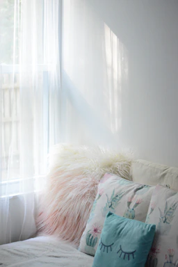 A cozy corner with a floral decor pillow and a sheer curtain softly lit by natural light.