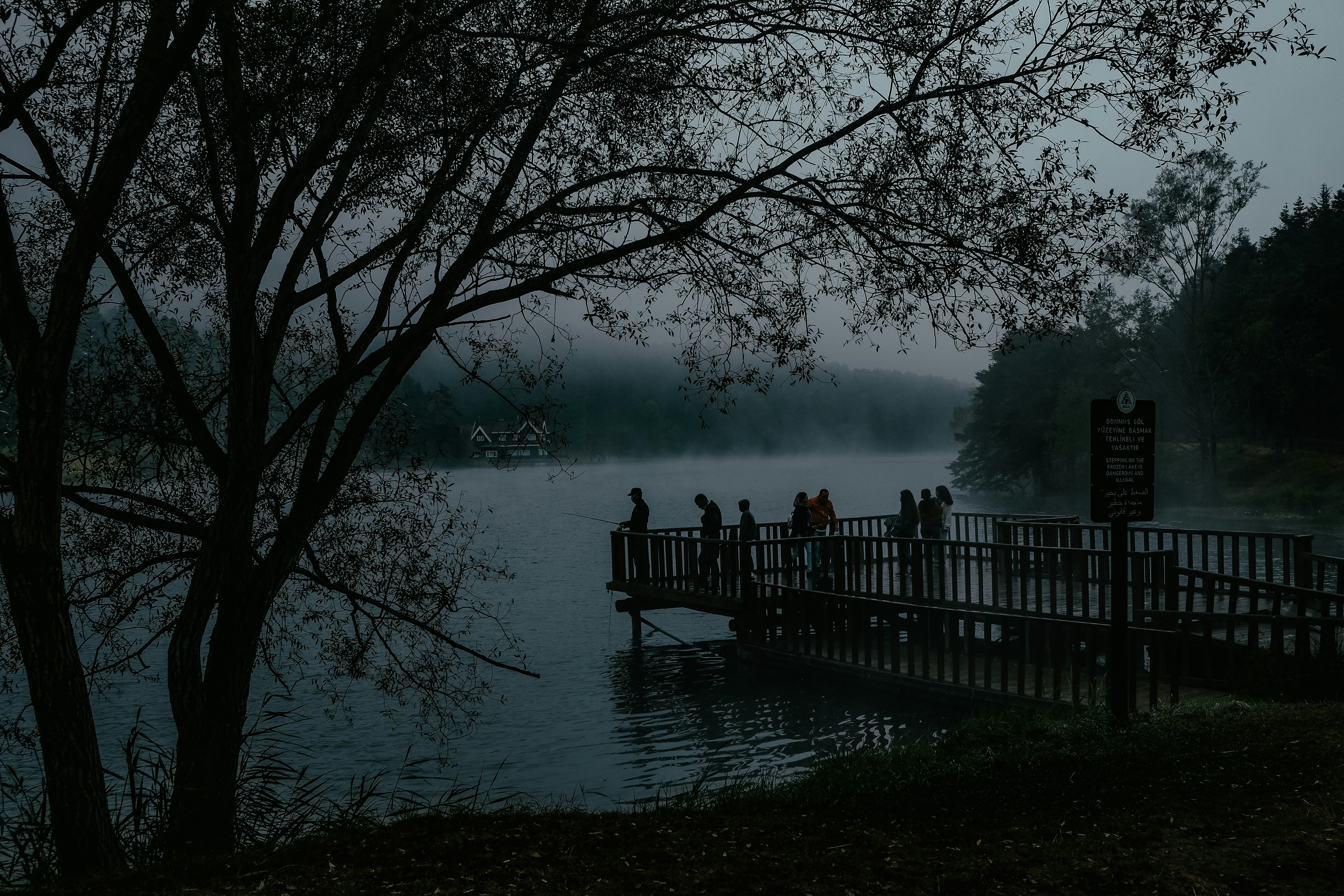 people standing on wooden bridge over body of water during foggy weather