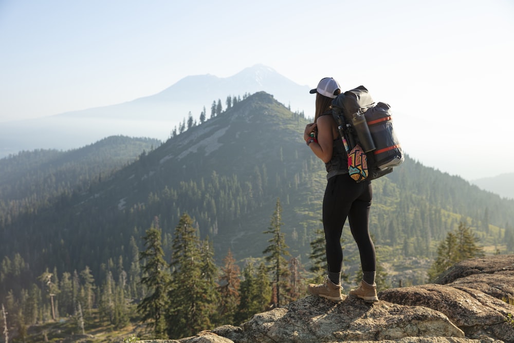 Mann in schwarzer Jacke und schwarzer Hose trägt schwarzen Rucksack, der tagsüber auf dem Rocky Mountain steht