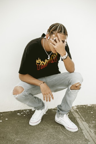 man in black crew neck t-shirt and blue denim jeans sitting on concrete floor