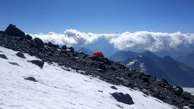 Spacious alpine tent pitched on a rocky terrain with snow-capped mountains in the background.
