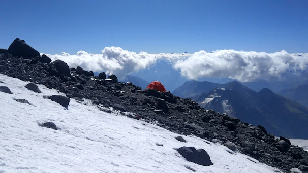 Spacious alpine tent pitched on a rocky terrain with snow-capped mountains in the background.