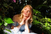 A serene image of a woman smiling gently, framed by natural sunlight and greenery.