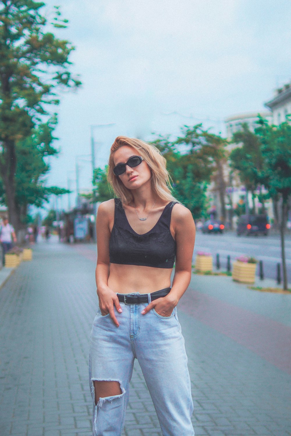 woman in black tank top and blue denim jeans wearing sunglasses standing on road during daytime