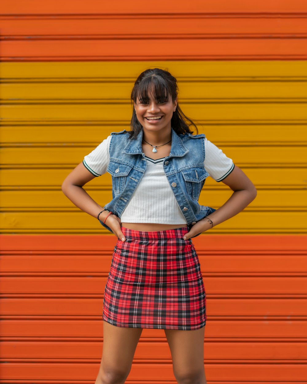 woman in white button up shirt and red and white plaid skirt standing beside yellow wall