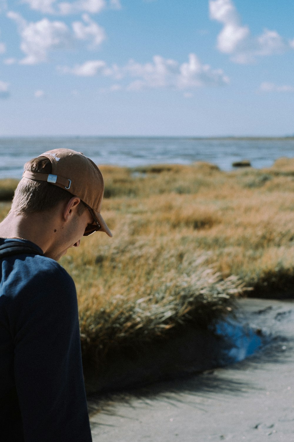 man in black hoodie wearing brown cap standing near body of water during daytime