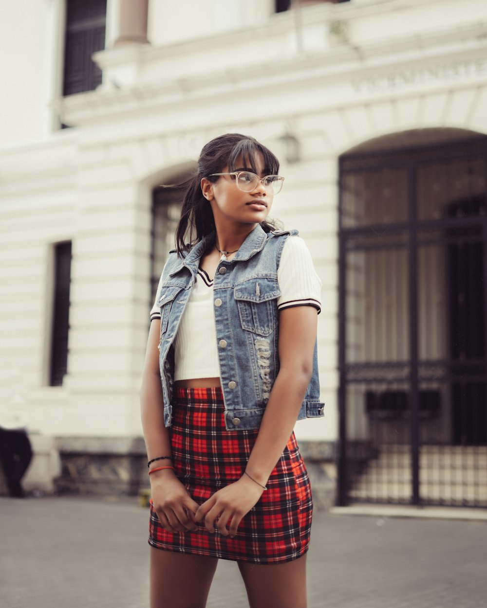 woman in blue denim button up jacket and red and black plaid skirt standing on sidewalk