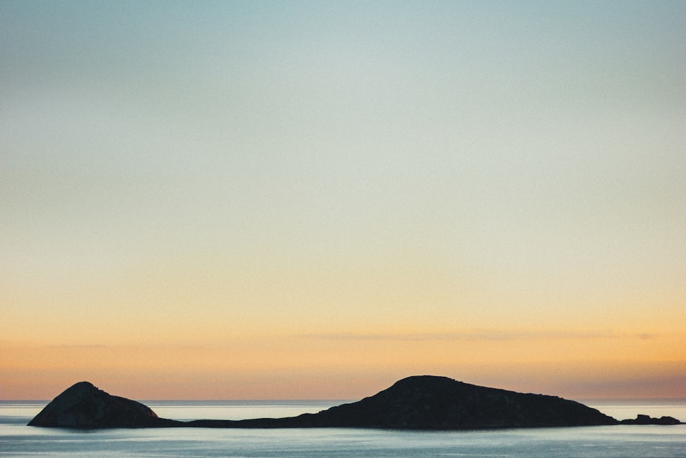 silhouette of mountain near body of water during sunset