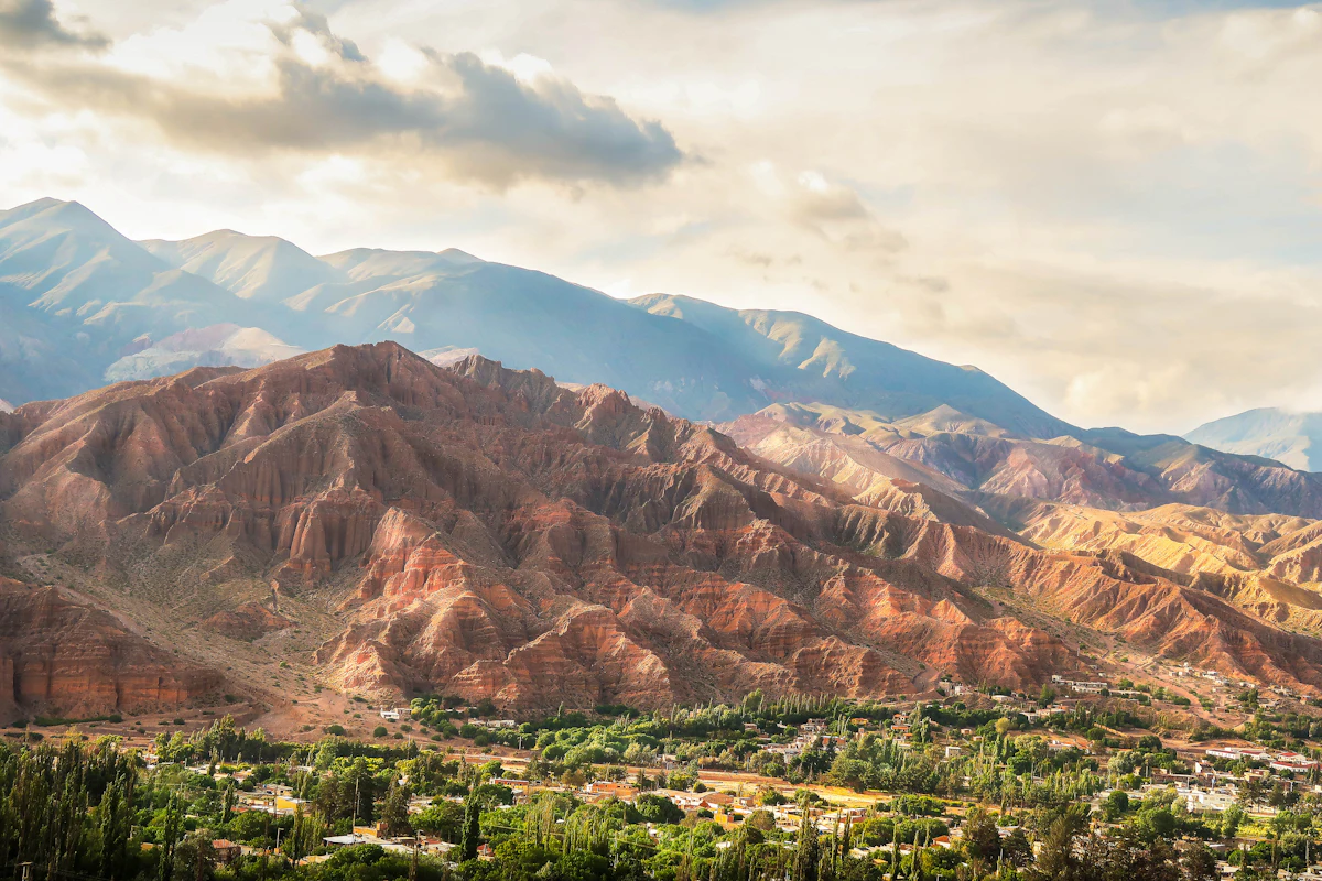 Red eroded hills above the green valley floor at Tilcara, with higher peaks behind