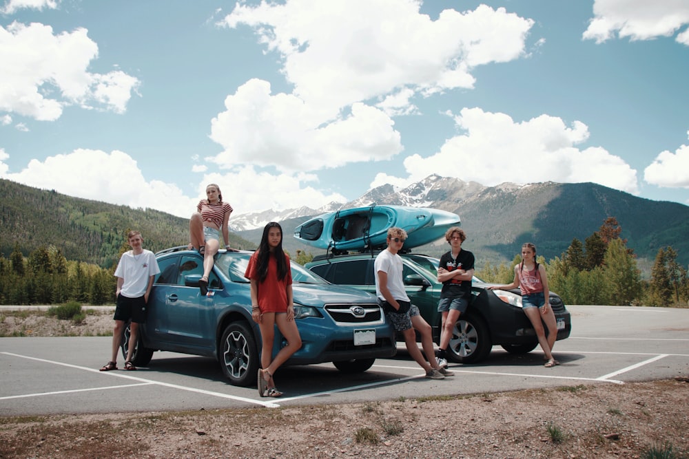 group of people standing beside blue car during daytime