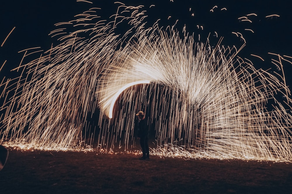 man standing on sand with fireworks display during night time