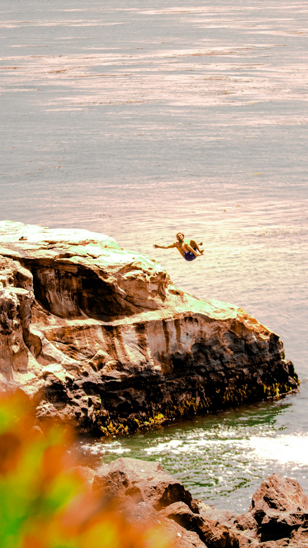 man in black shorts jumping on brown rock formation during daytime