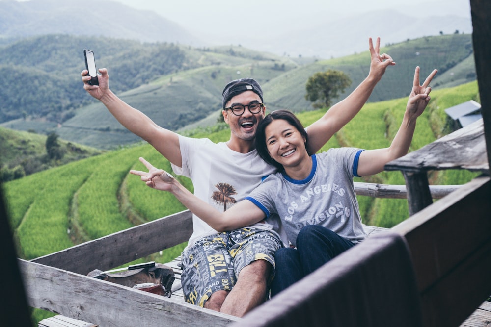 man and woman sitting on brown wooden fence during daytime