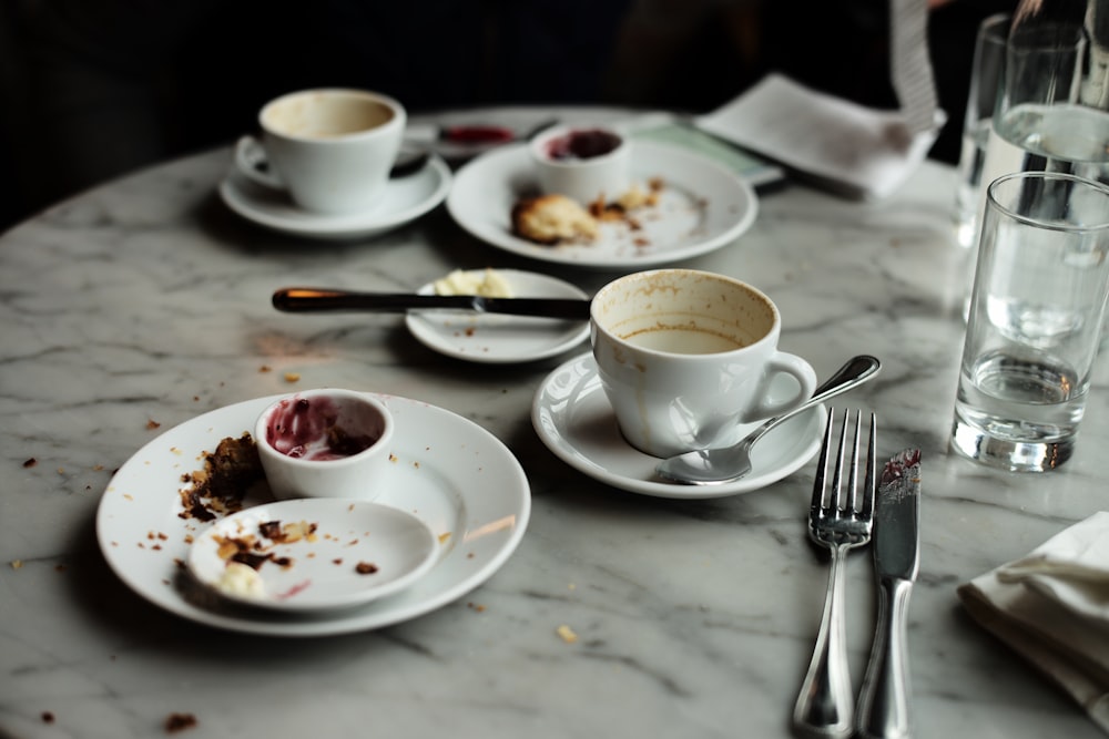 white ceramic teacup on saucer beside stainless steel spoon and fork