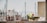 A construction worker wearing a fluorescent safety jacket and red helmet is working near a concrete structure. In the background, there are several unfocused yacht masts and indistinct buildings, suggesting a marine or port environment.