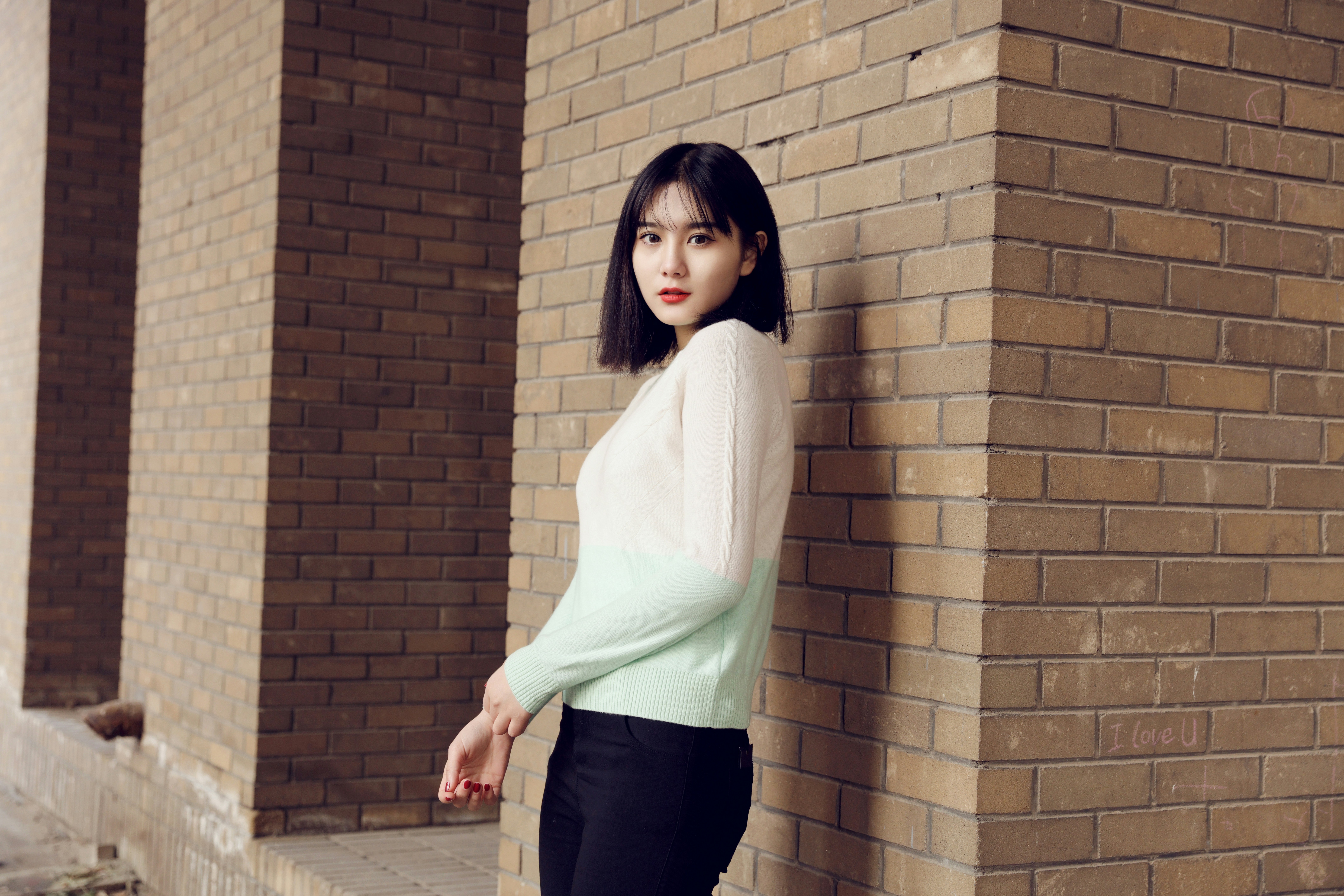 woman in white long sleeve shirt and black pants standing beside brown brick wall