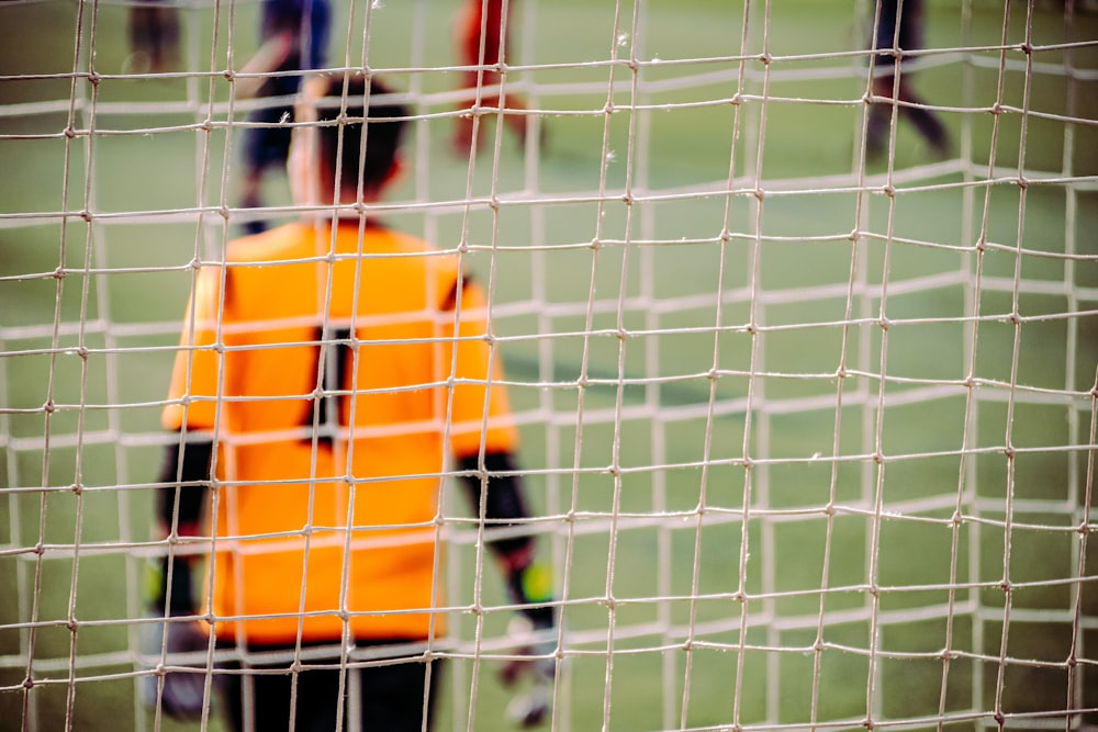 hombre con camisa de manga larga naranja y negra de pie en el campo de fútbol