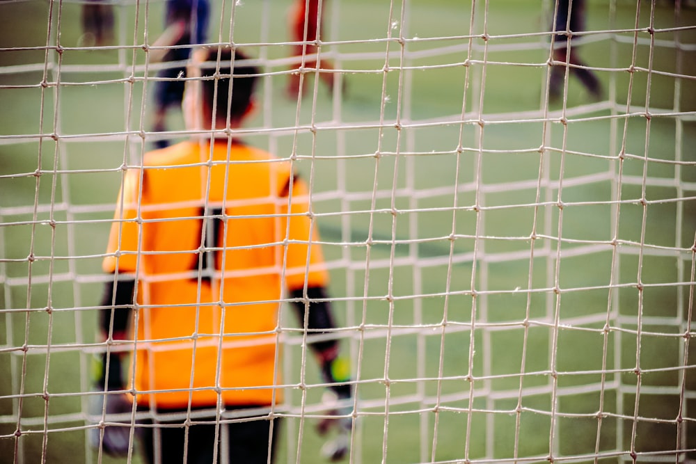 man in orange and black long sleeve shirt standing on soccer field