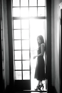 A side profile of a woman in a flowing black dress, her silhouette highlighted by natural light through a large window.