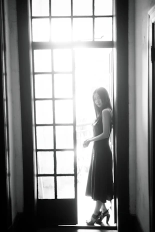 A side profile of a woman in a flowing black dress, her silhouette highlighted by natural light through a large window.