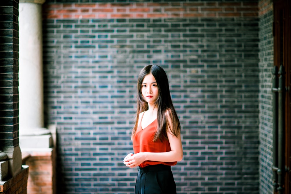 woman in orange tank top and black skirt standing beside brick wall
