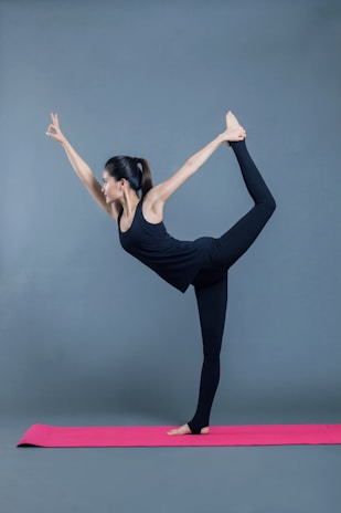 A woman gracefully holding a pilates pose on a cream-colored mat, dressed in minimalistic blush pink athleisure.