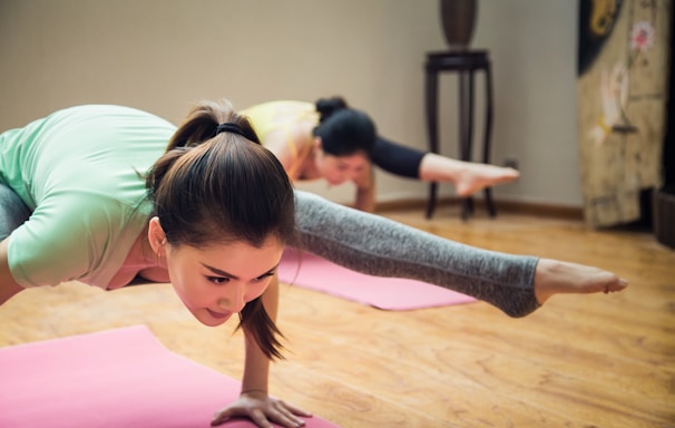 girl in green t-shirt and gray pants doing yoga on pink yoga mat