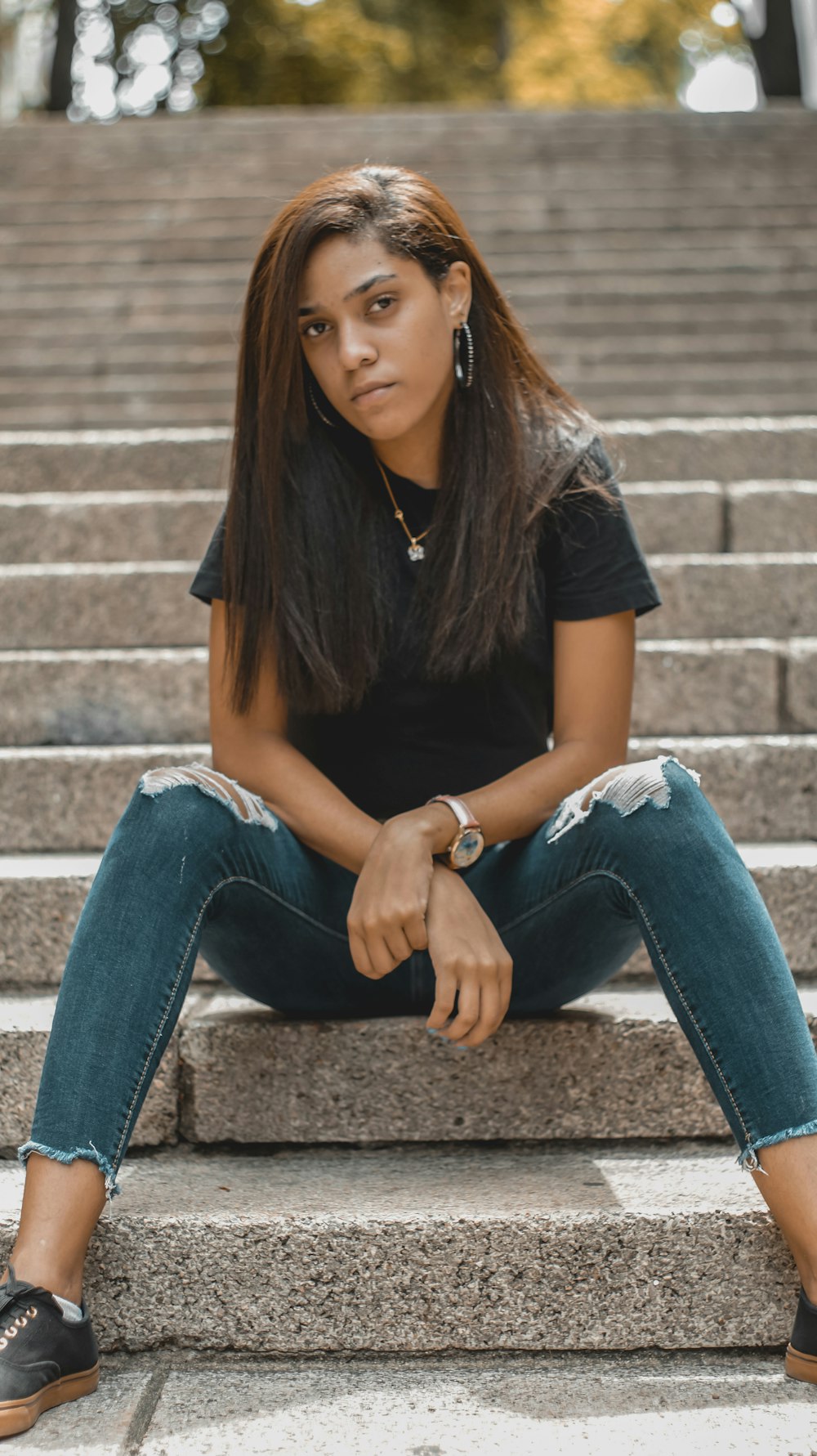 Mujer con camisa negra y jeans de mezclilla azul sentada en escaleras de concreto marrón