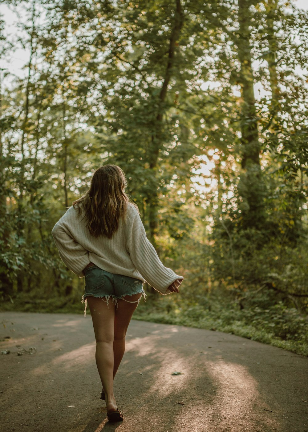 woman in gray long sleeve shirt and blue denim shorts walking on pathway between trees during