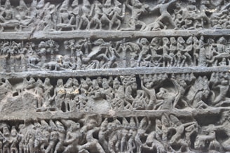 Intricate stone carvings depict various human and mythical figures engaged in dynamic scenes. The figures are in detailed relief, showcasing activities and expressions that suggest a narrative. The carvings are organized into distinct horizontal sections, each illustrating different aspects of the story.