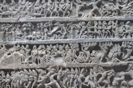 Intricate stone carvings depict various human and mythical figures engaged in dynamic scenes. The figures are in detailed relief, showcasing activities and expressions that suggest a narrative. The carvings are organized into distinct horizontal sections, each illustrating different aspects of the story.