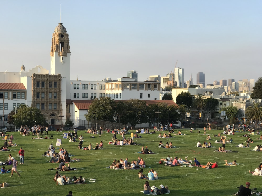 people sitting on green grass field near white concrete building during daytime