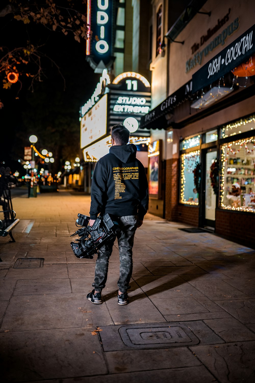 homem em camisa preta de manga comprida e calças pretas em pé na calçada durante a noite