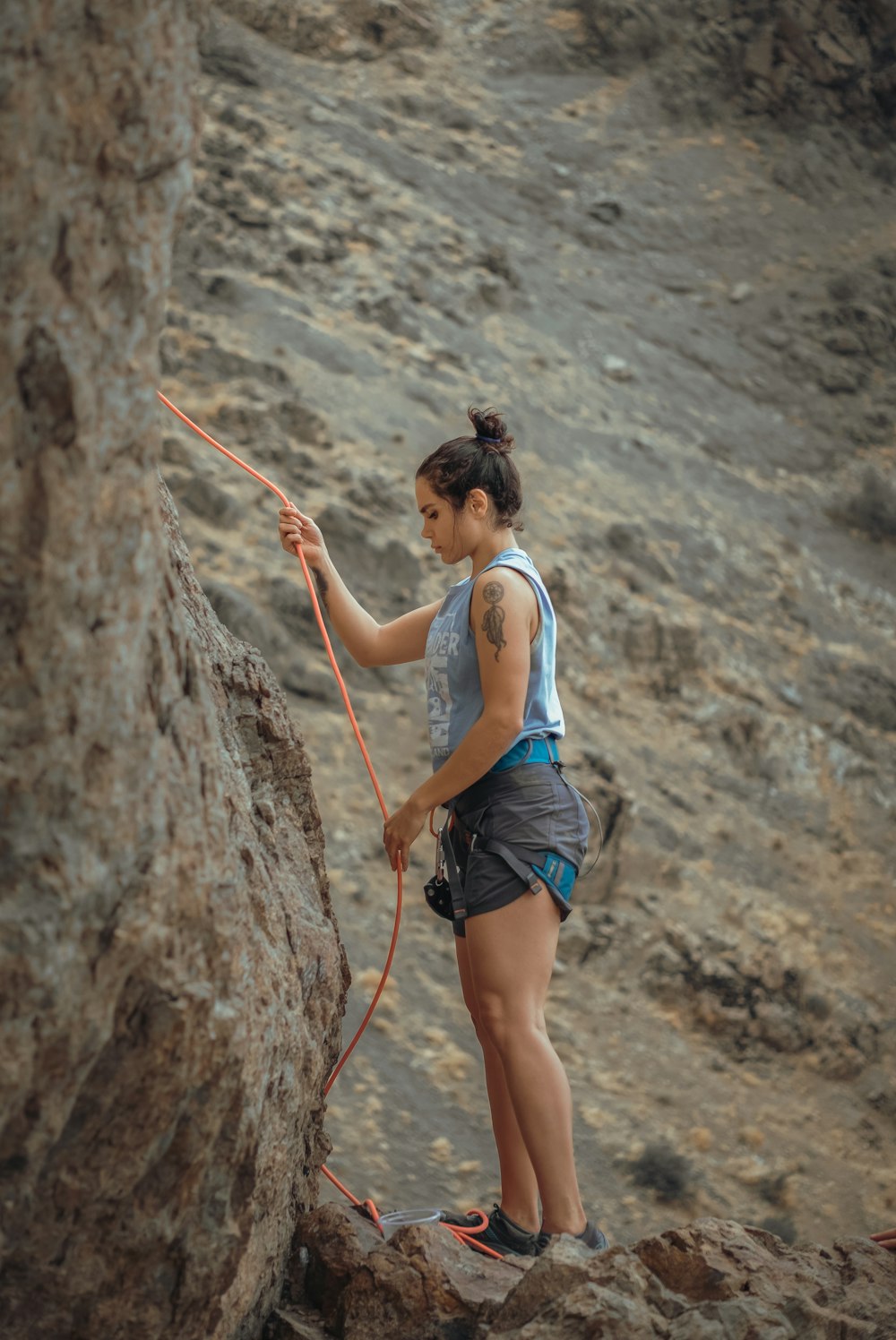woman in white tank top and blue denim shorts climbing on brown rock during daytime